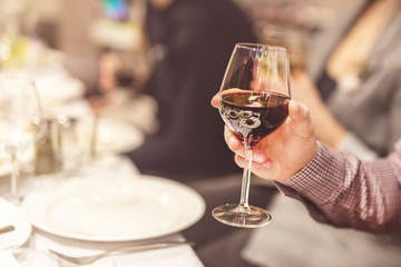 Adult hand holding glass of red whine. Toasting at celebration . Cafe or restaurant background.  Chief speech while corporate business party