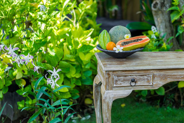 Fruit plate with fresh Bali fruits papaya, orange, melon and star fruit on wooden vintage table in tropical garden. Frangipani flowers