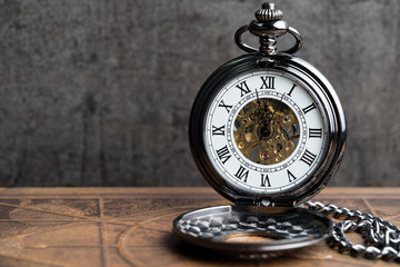 Time symbol or business deadline countdown concept, closed up vintage pocket watch on brown old book with black dark cement wall