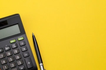 Flat lay or top view of black pen with calculator on vivid yellow background table with blank copy...