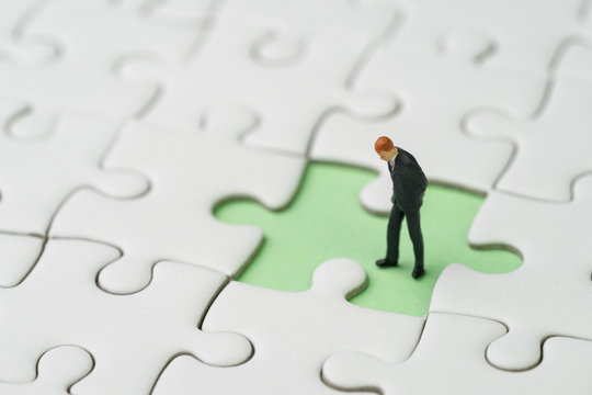 Finding the missing piece for business success concept, miniature people businessman standing and looking at the missing white jigsaw puzzle piece on pastel green background