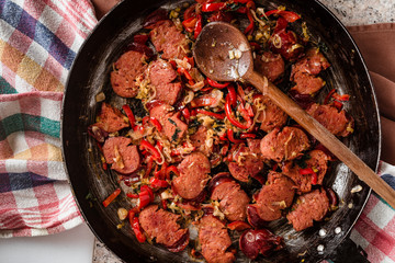 Sliced sausage and mix of fresh vegetables fried in the rustic pan with scoop on dishcloth.
