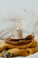 Coffee cup placed on a wooden tray and warm sweater with background bokeh blur of lights. Morning in Bed. Still Life Composition with Copy Space