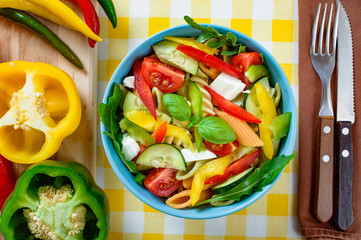Pasta salad with tomato,arugula, cucumber, peppers,hot peppers, black and green olives, and cheese feta.  Top view.