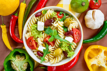 Pasta salad with tomato,arugula, cucumber, peppers,hot peppers, black and green olives, and cheese feta.  Top view.