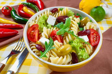 Pasta salad with tomato,arugula, cucumber, peppers,hot peppers, black and green olives, and cheese feta.  Top view.