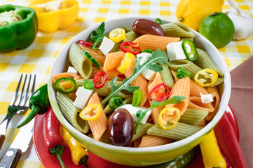 Pasta salad with tomato,arugula, cucumber, peppers,hot peppers, black and green olives, and cheese feta.  Top view.