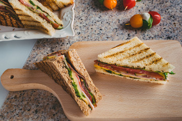 Club sandwich with ham, salami, smoked beef, cheese, lettuce and arugula.  Top view.  Caprese salad...