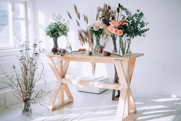 a wooden table with a side on which there are roses, dried flowers of cones and greens against a white wall with voluminous light