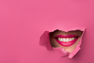 close-up of female lips with pink lipstick and a broad smile that peeps through the pink torn paper - obrazy, fototapety, plakaty