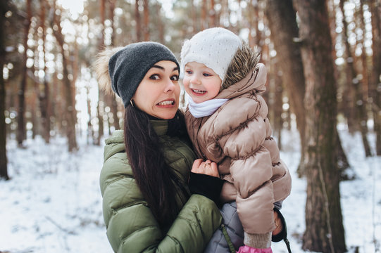 A beautiful young mother and her little adorable daughter laugh and funny. Comic, joke picture. Grimace. Winter forest, snow.