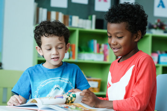 American and African boys are reading together with happiness in their kindergarten classroom, kid education and diversity concept