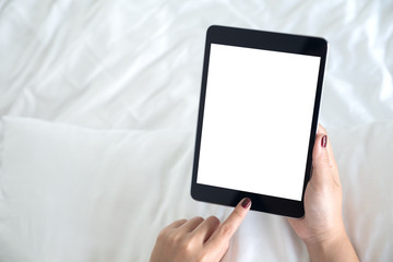 Top view mockup image of hands holding and using a black tablet pc with blank desktop white screen on a white bed background