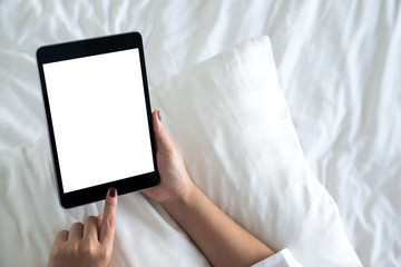 Top view mockup image of hands holding and using a black tablet pc with blank desktop white screen on a white bed background