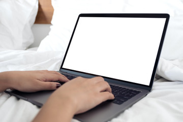 Mockup image of hands using and typing on laptop with blank white desktop screen keyboard on bed