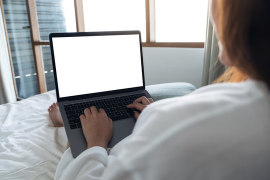 Mockup image of a woman sitting in a bed , using and typing on laptop with blank white desktop screen keyboard