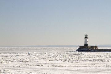Person walkingon frozen Lake Superior along pier with lighthouse in Duluth, Minnesota