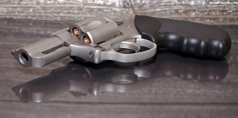 A loaded, stainless steel .357 magnum revolver on a reflective surface with a wooden background