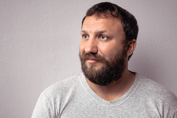 Obraz premium Happy bearded man in gray t-shirt looking away while standing against gray wall.