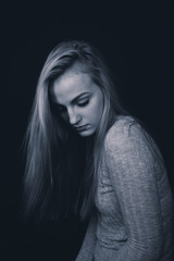 Teenage girl with long blond hair looking down, sitting in the shadows.