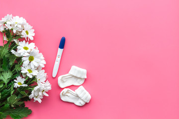 Obraz na płótnie Canvas Joy of long-awaited pregnancy. Pregnancy test with two stripes near flowers on pink background top view copy space