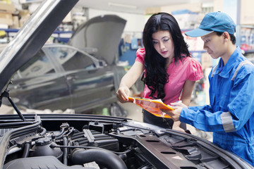 Car mechanic helps a customer standing next to the serviced car and looking through the checklist.