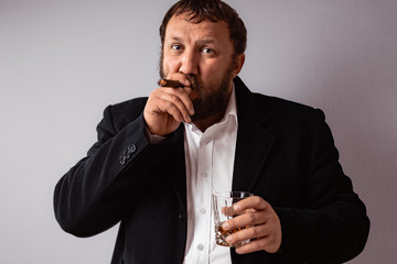 Bearded man in modern coat and shirt smoking his cigar and drink some strong liquor toast and celebrating.