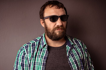 Obraz premium Handsome hipster bearded man with sunglasses and shirt standing against dark gray wall.
