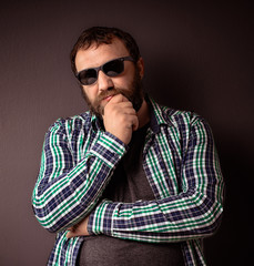 Obraz premium Handsome hipster bearded man with sunglasses and shirt holding hand on his beard.