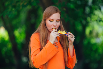 Portrait of pretty red hair woman with juicy delicious orange at summer green park.