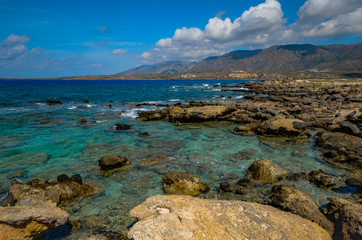 Fototapeta na wymiar the rocky shore of the sea. the turquoise sea and mountains on a blue sky background with clouds. Elafonisi, Crete, Greece