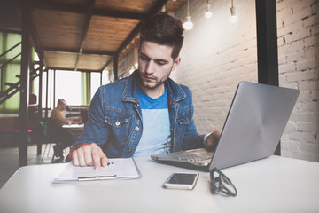 Young businessman working in office, sitting at desk, looking at laptop computer screen, smiling