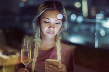 Serious young woman using a smartphone at a rooftop bar in the evening