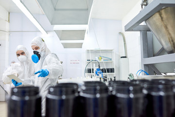 Naklejka premium Team of confident factory workers wearing rubber gloves and coveralls using digital tablet in order to take notes while taking inventory in sport nutrition factory