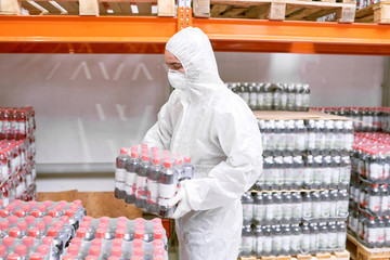 Profile view of male worker wearing coverall and safety mask carrying soft drink bottles in plastic...