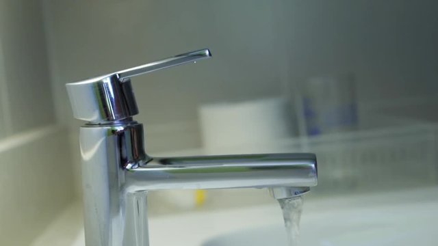 Close up on chrome faucet with water flowing and child hand turn off chrome faucet in the bathroom