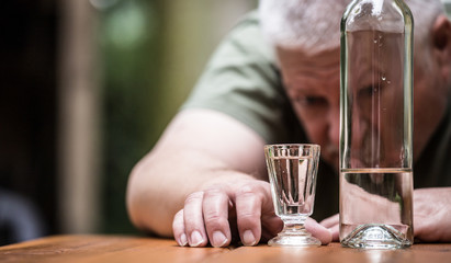 ein betrunkener Mann sitzt an einem Tisch, vor ihm stehen eine Flasche und ein Glas mit Alkohol