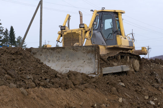 The yellow tractor with attached grederom makes ground leveling. Work on the drainage system in the field.