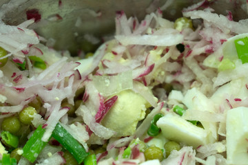potato salad with fresh radishes in a white bowl on a rustic wooden table.