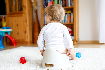 Closeup of legs of cute little 12 months old toddler baby girl child sitting on potty. - obrazy, fototapety, plakaty
