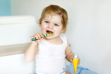 Little baby girl holding toothbrush and brushing first teeth. Toddler learning to clean milk tooth.