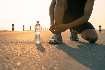 Male runner tying shoes in preparation for a run in the morning and bottle water. The concept of...