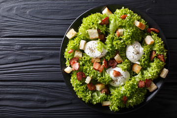Gourmet salad Lyonnaise with lettuce, crispy bacon, croutons and poached eggs close-up on a plate. horizontal top view