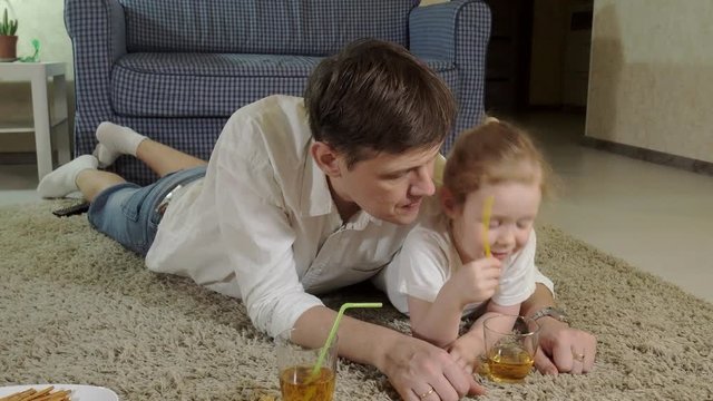 man and daughter watching television, sitting on the floor drink juice