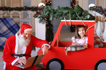 Father Christmas writing letters on laptop. Beautiful princess enjoying with presented tablet....