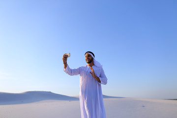 Happy, handsome guy, emirate and tourist, conducts dialogue through Internet with help of device,...