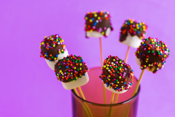 marshmallows on a sticks on pink background. glazed with chocolate and colorful sprinkles.