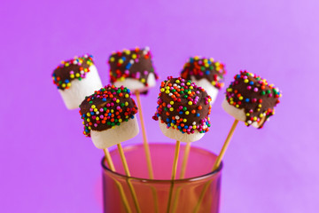 marshmallows on a sticks on pink background. glazed with chocolate and colorful sprinkles.