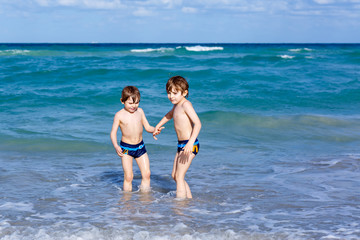 Two kid boys running on ocean beach. Little children having fun