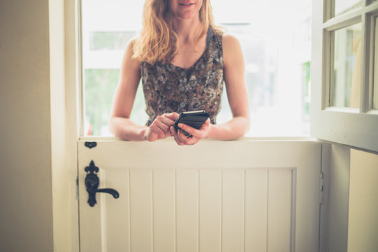 Young woman with phone by stable door